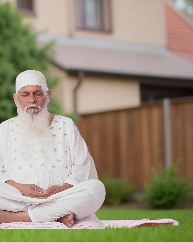 Swamiji seated in meditation on a lawn beside a Dhyanasthali building