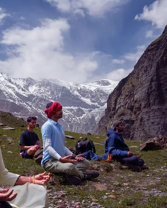 Practitioners meditating on a mountainside beneath snow peaks