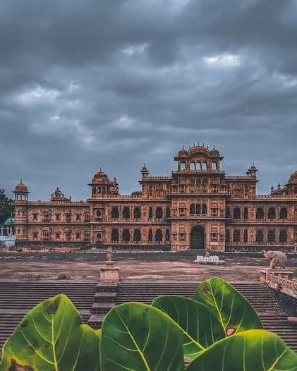 A sandstone palace beneath monsoon clouds, framed by large leaves