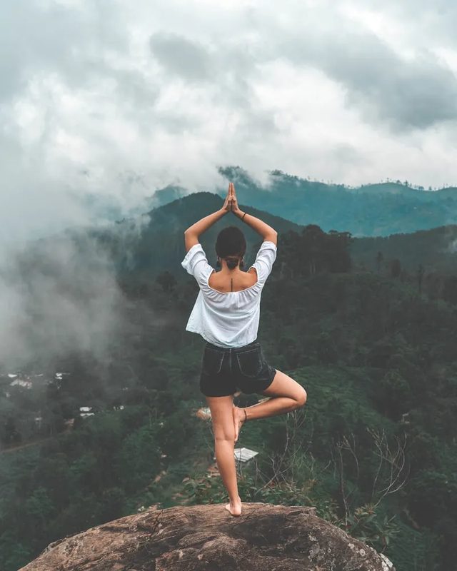 A person balancing in a yoga pose on a rock above misted hills